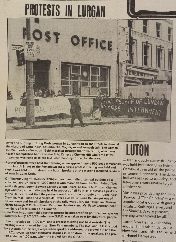 Black and white image of a protest in Lurgan, with demonstrators holding banners near a post office. The banners read 'The People of Lurgan Oppose Internment' and 'Release the Political Hostages'.